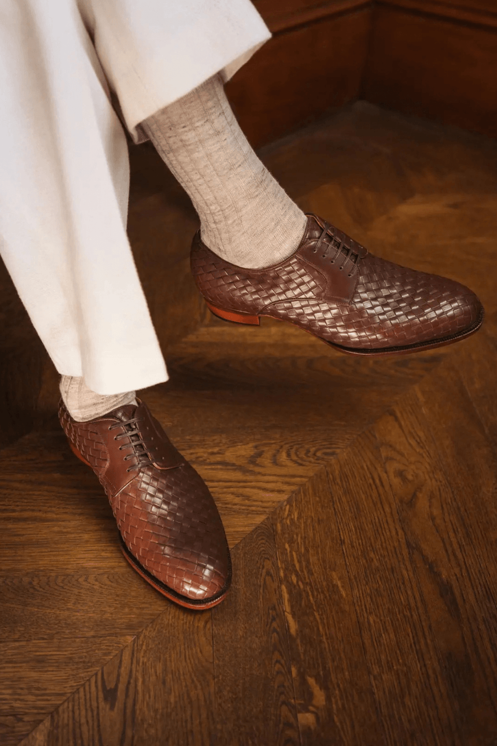 A close-up of a person's feet wearing dark brown woven leather shoes and light gray socks.