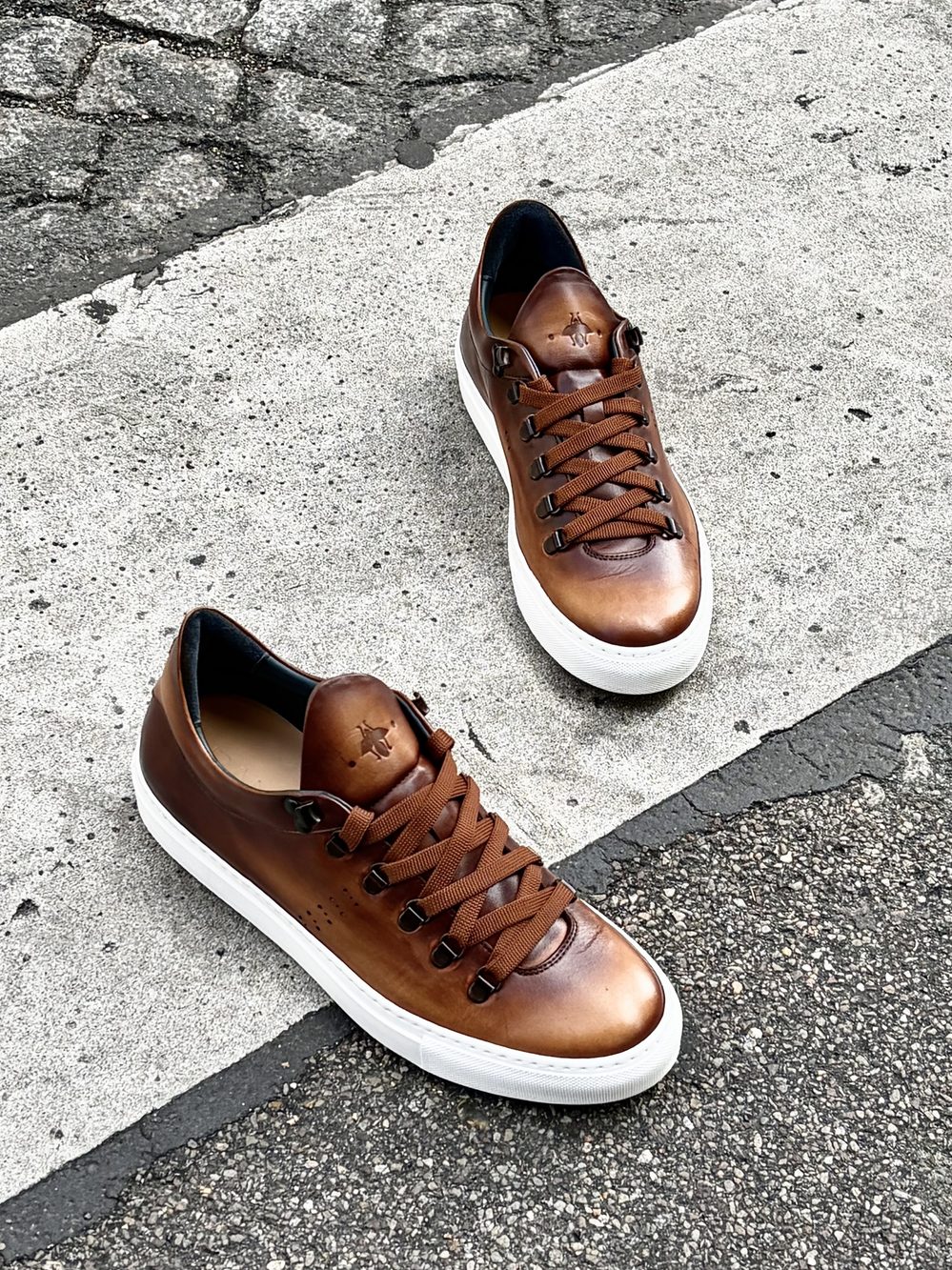 A pair of brown leather sneakers with white soles and brown laces.