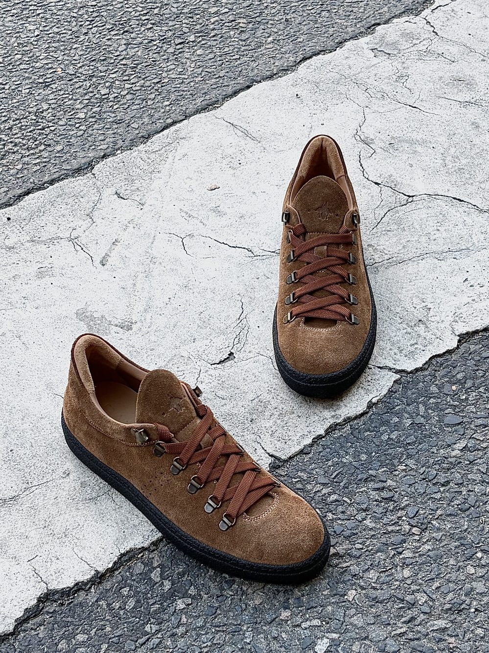 A pair of brown suede sneakers with brown laces and black rubber soles.