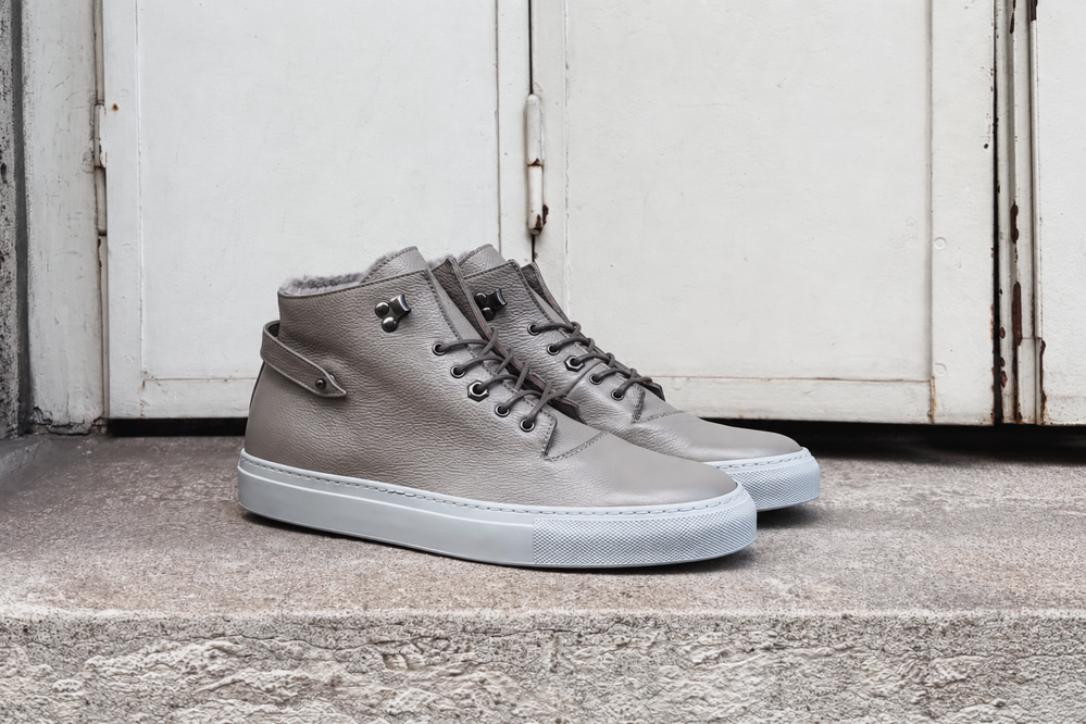 A pair of gray leather high-top sneakers with a white sole displayed on a stone surface.