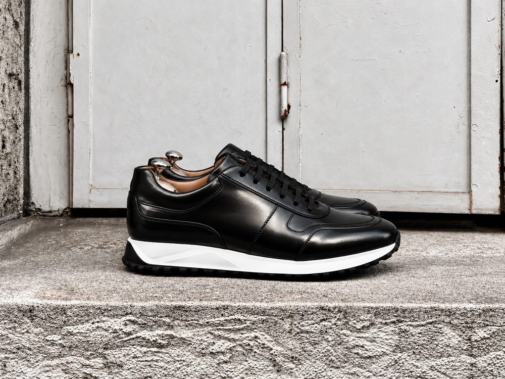 A pair of black leather sneakers with white soles and black rubber treads.