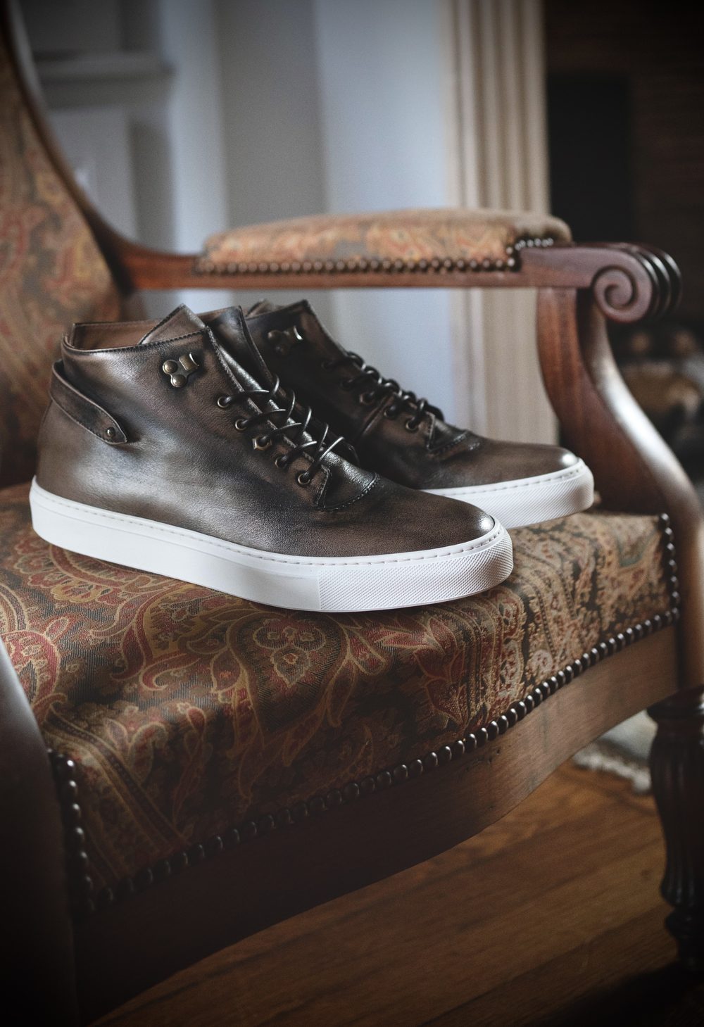 A pair of brown leather high-top sneakers with white soles resting on a patterned chair.