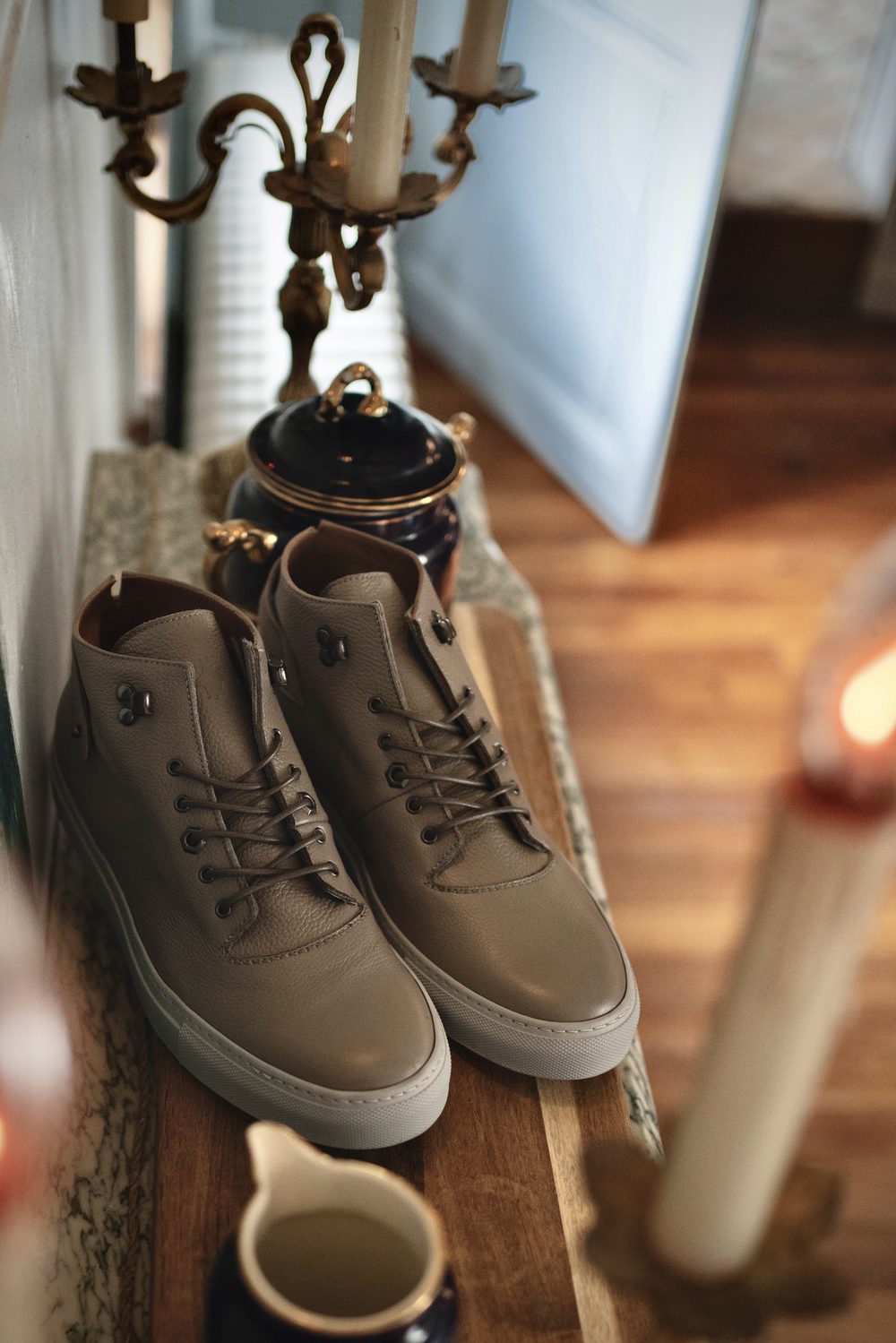 A pair of taupe leather sneakers with brown accents and laces is displayed on a wooden surface.