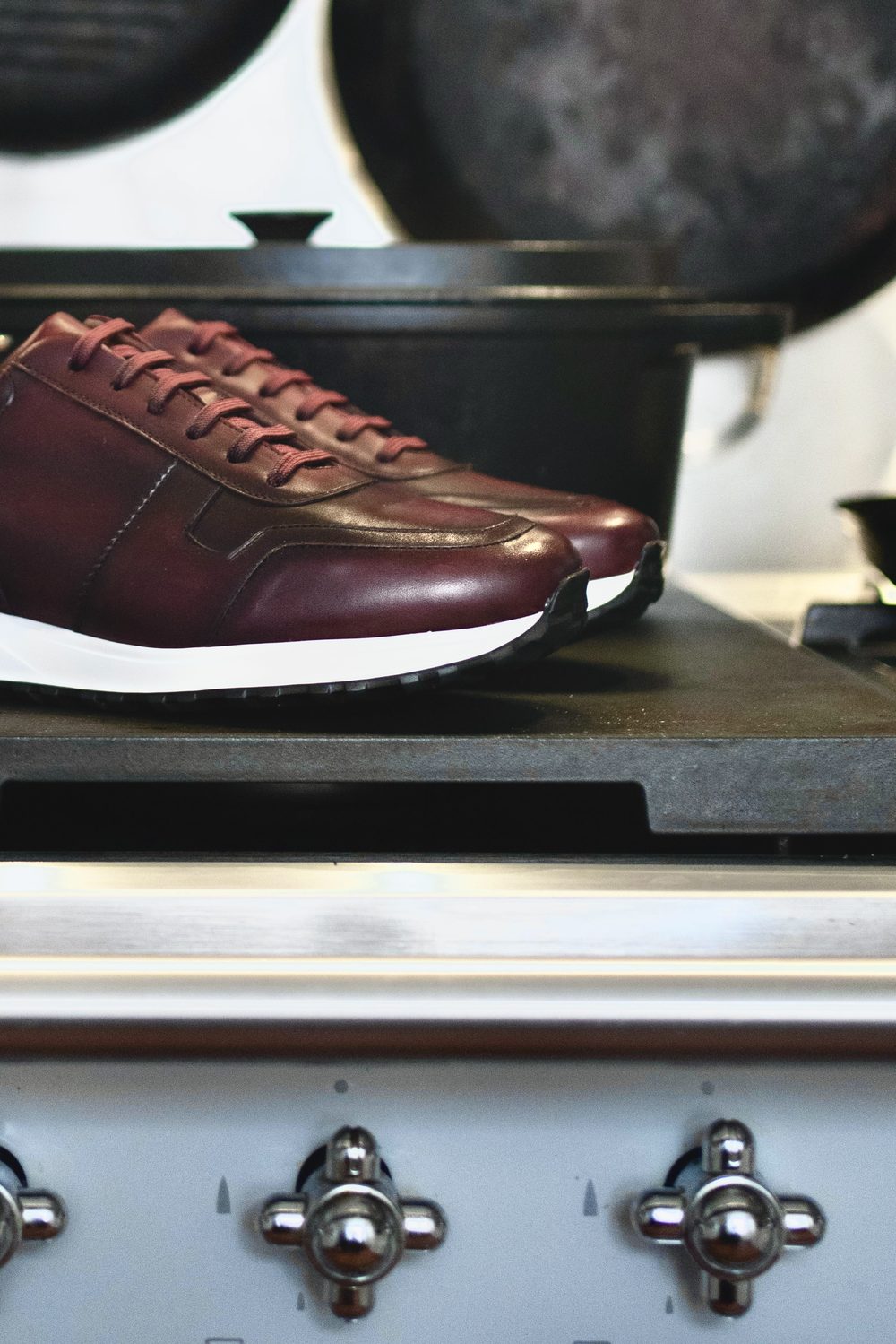 A pair of burgundy leather sneakers with white soles, positioned on a dark surface.