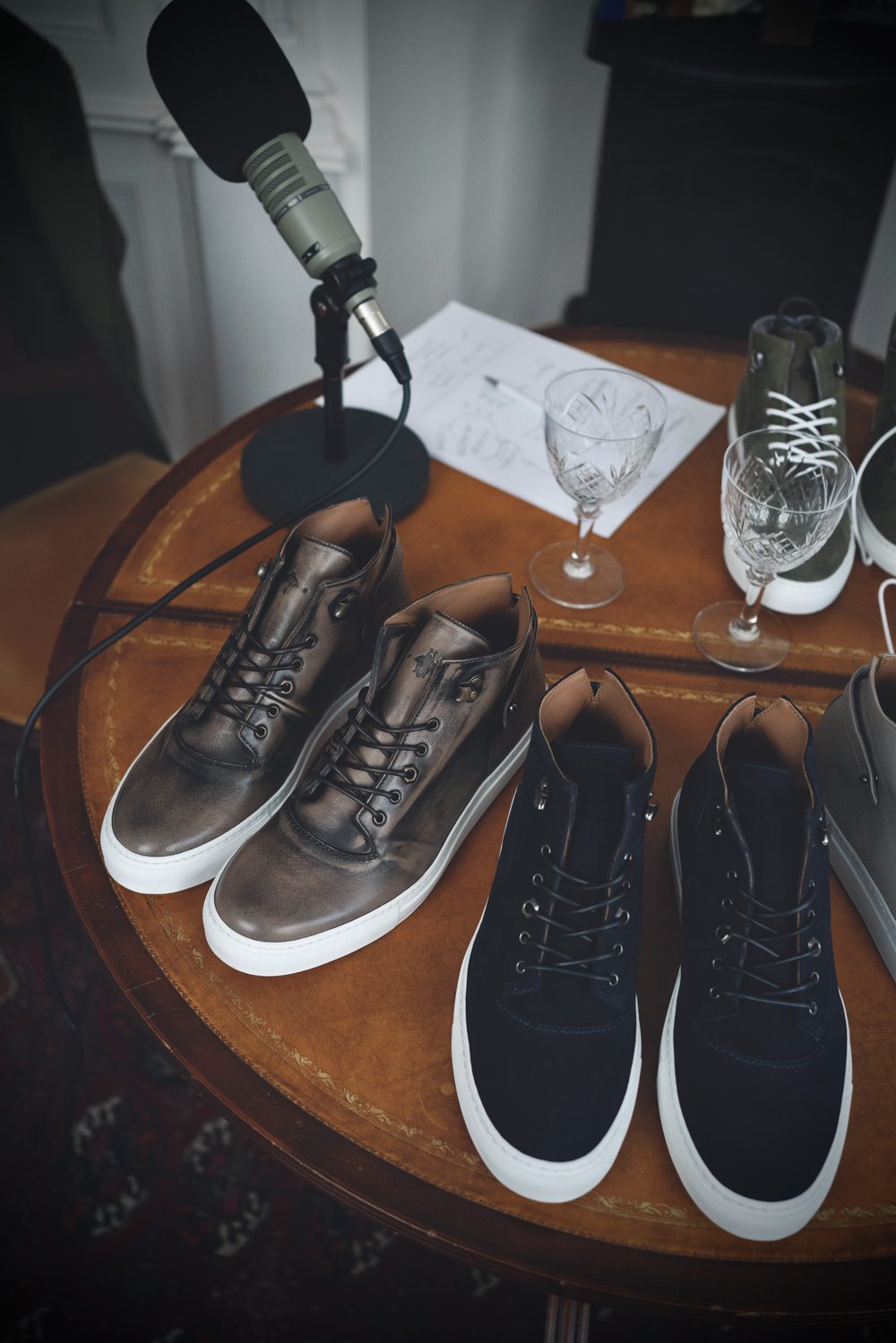 Two pairs of stylish sneakers in brown leather and navy suede, displayed on a wooden table.