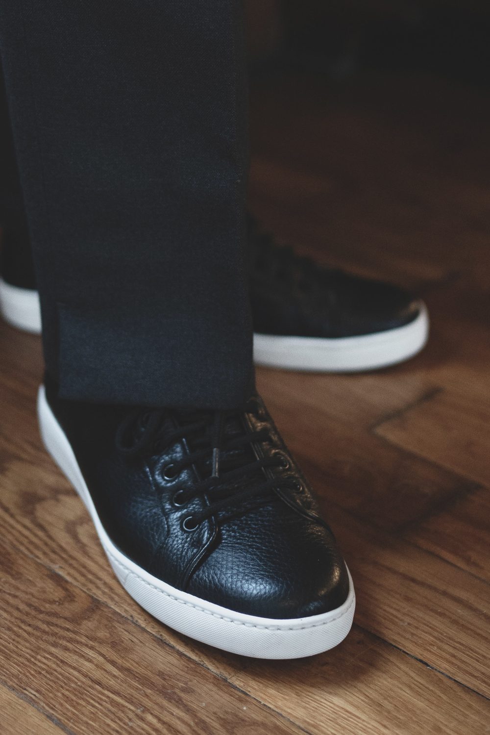 Black leather sneakers with white soles, worn with dark trousers.