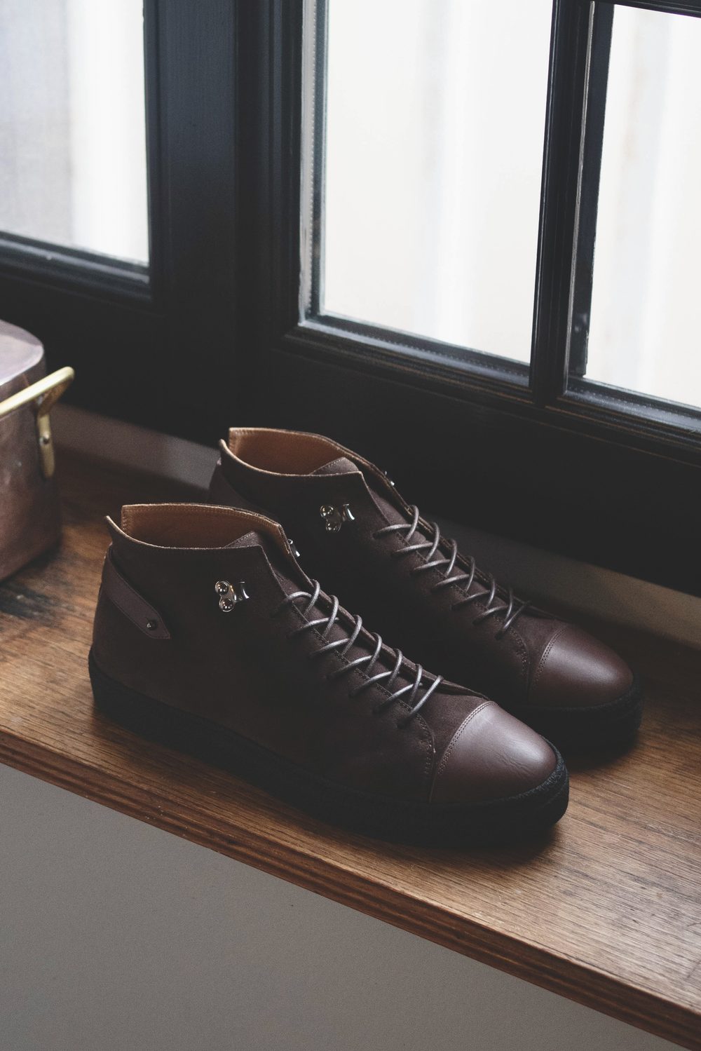 A pair of brown leather high-top sneakers with laces and metallic accents on a wooden surface.