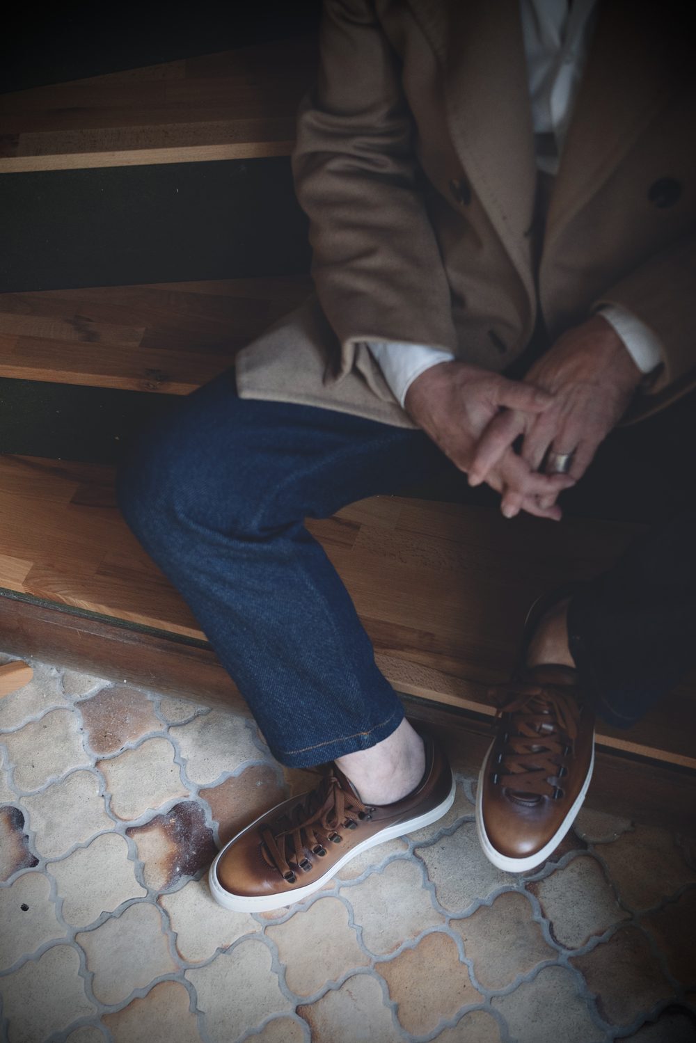 A close-up of brown leather sartorial sneakers worn with dark denim trousers.