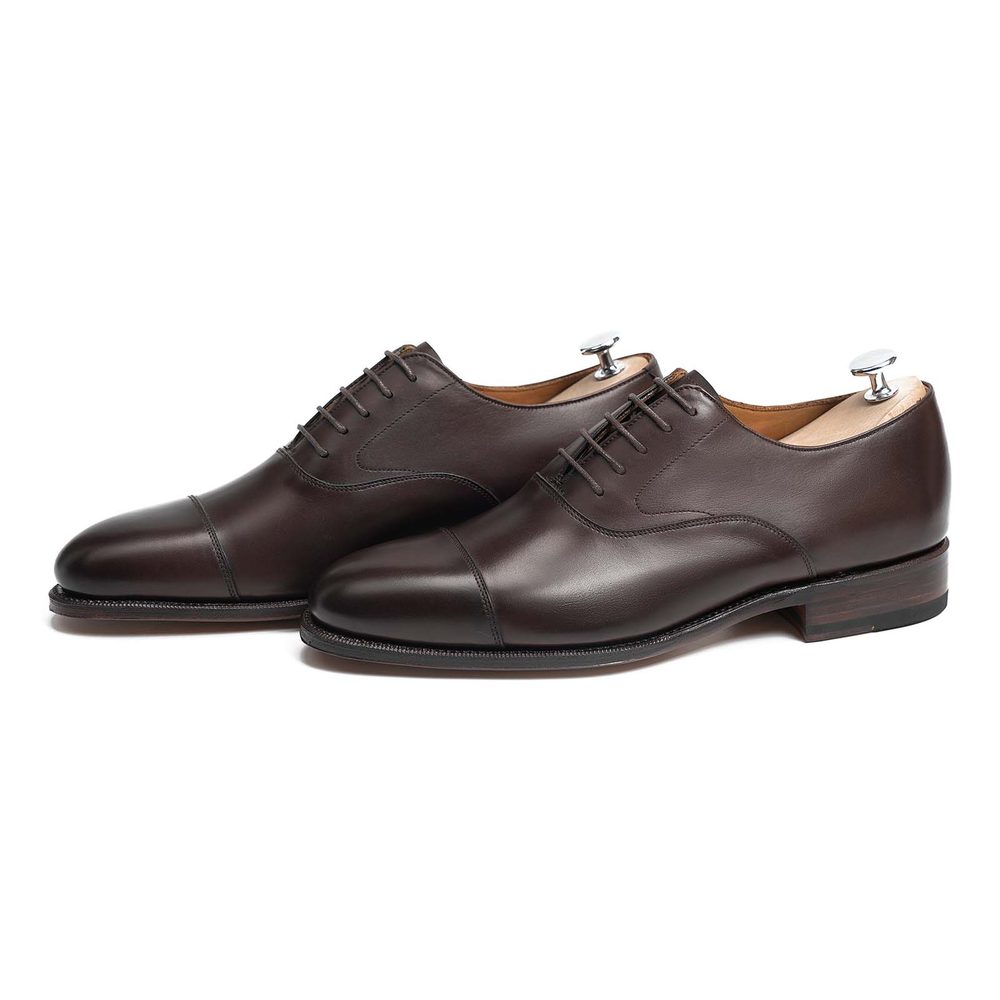 A pair of dark brown leather dress shoes with a cap-toe design and metal shoe trees.