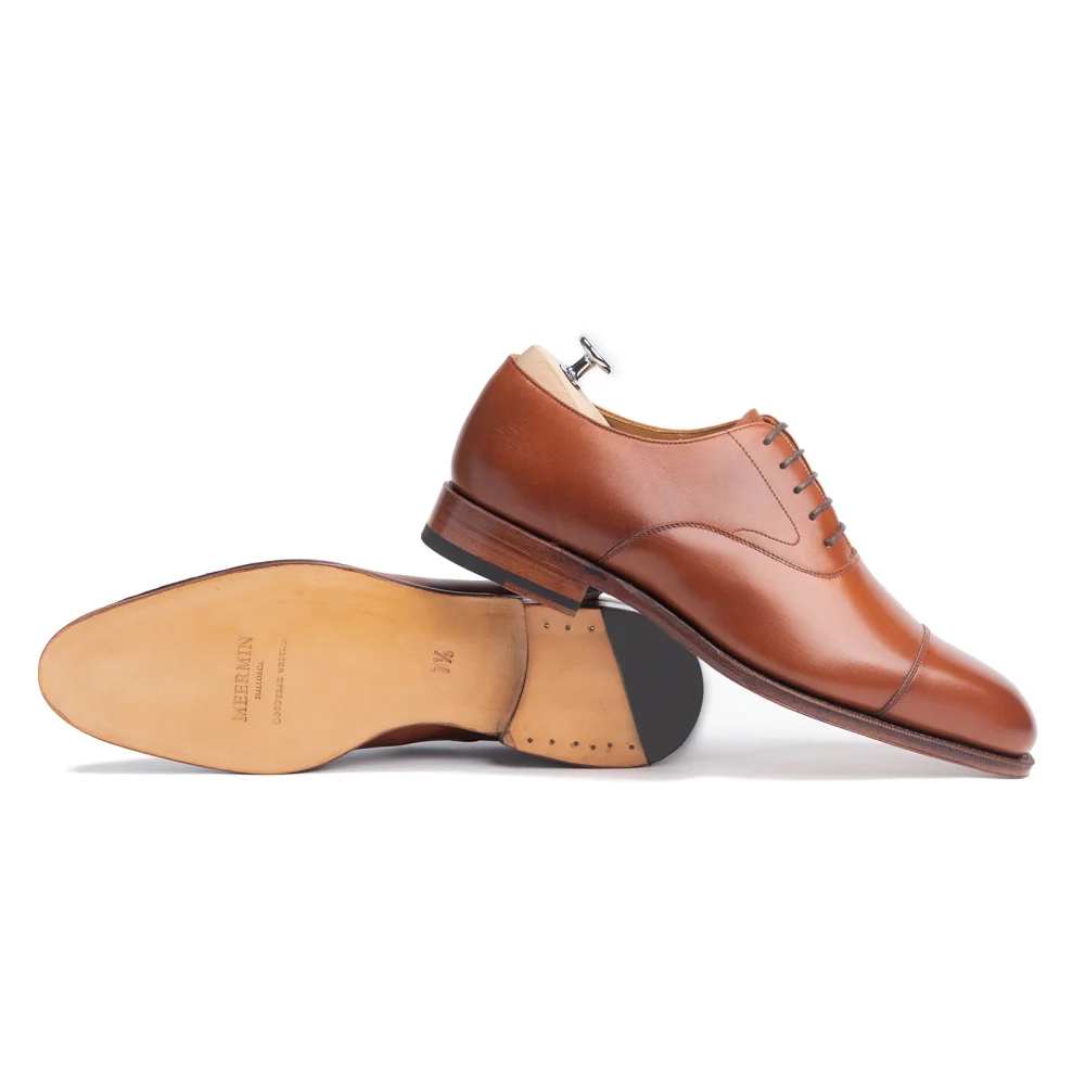 A pair of brown leather dress shoes with laces and a shoe tree inserted in one.
