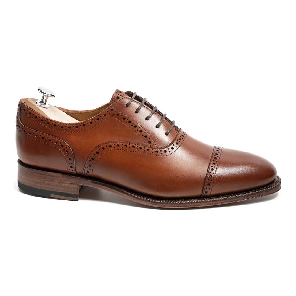 A brown leather dress shoe with decorative perforations and a wooden heel.