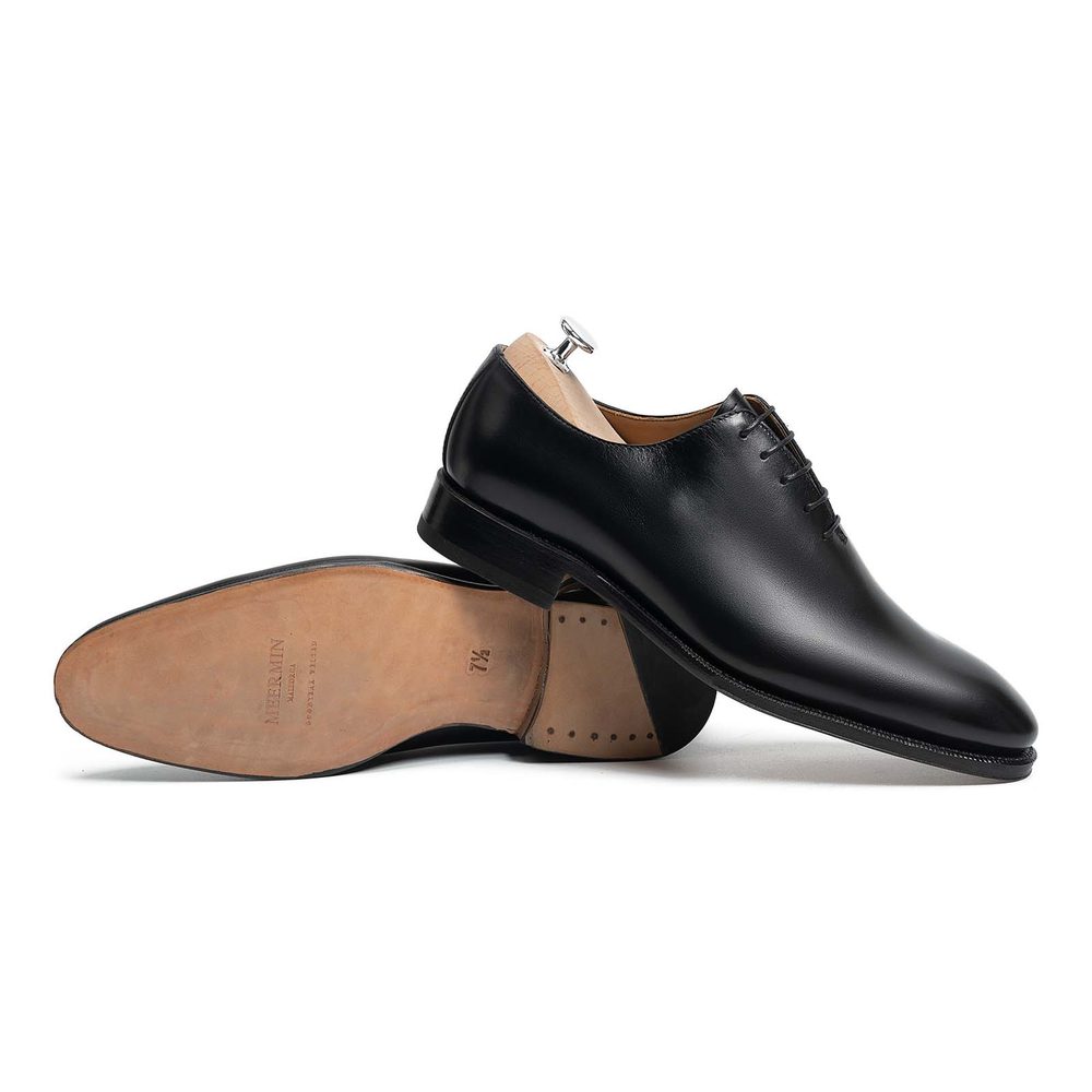 Black leather dress shoes with a smooth finish, featuring a lace-up design and a wooden shoehorn.
