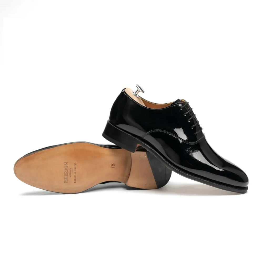 A pair of black patent leather dress shoes with a polished finish and a light-colored leather insole.