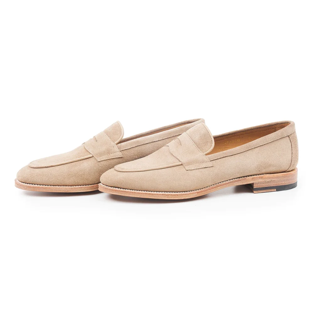 Beige suede loafers with a low heel and decorative stitching.