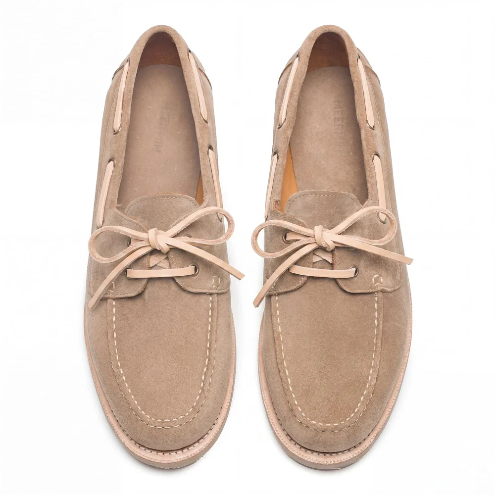 A pair of light brown suede shoes with leather laces and white stitching.