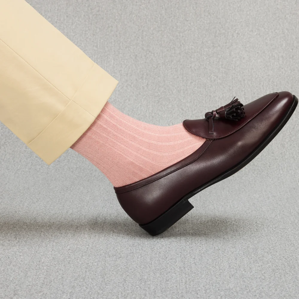 A foot wearing light pink ribbed socks paired with a dark brown leather loafer, illustrating the contrast in style for over the calf vs mid calf socks.