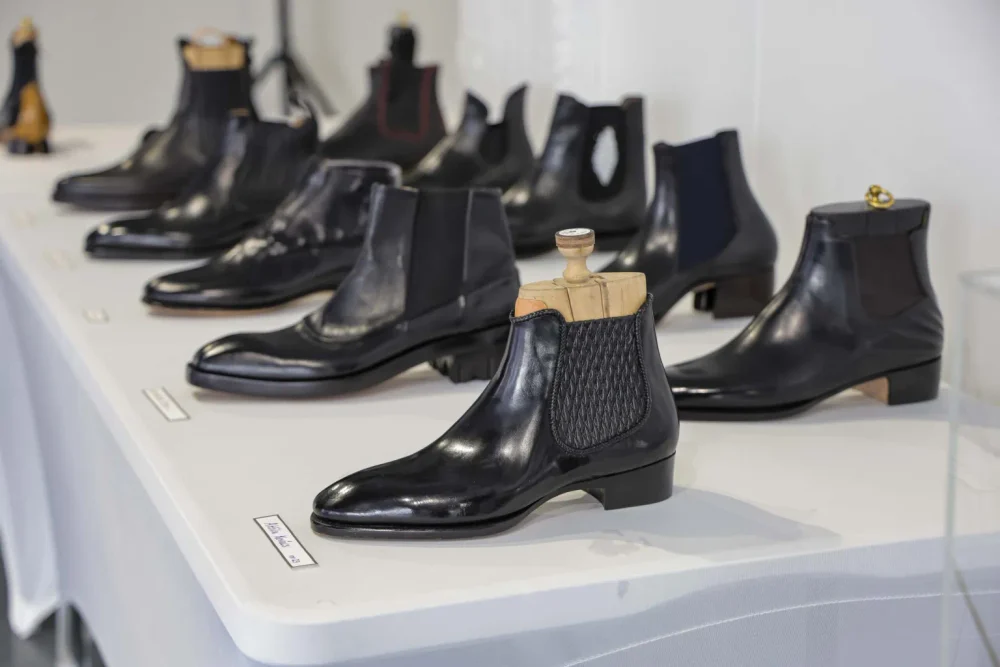 A row of black leather shoes, including a chelsea boot with a wooden shoe tree, displayed on a table.
