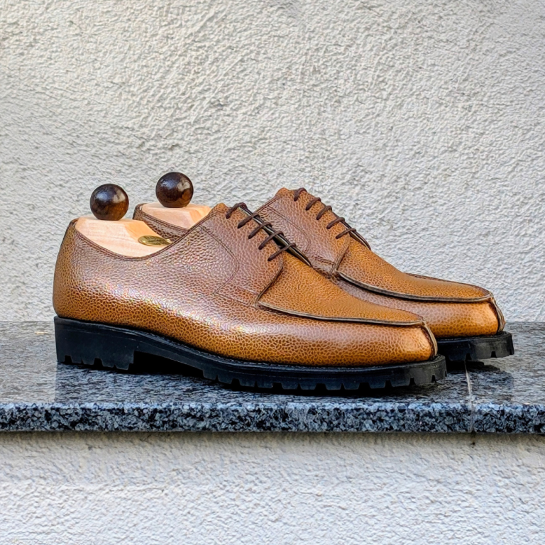 A pair of brown leather shoes with a textured finish and wooden shoe trees.