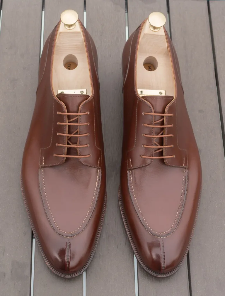 A pair of polished brown leather shoes with a classic lace-up design and wooden shoe trees inside.