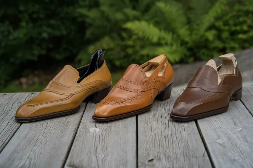 Three pairs of leather shoes in shades of tan and brown are displayed on a wooden surface.