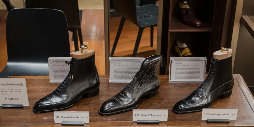 Three pairs of elegant black shoes are displayed, showcasing the top three winners of the World Championships of Shoemaking 2027.