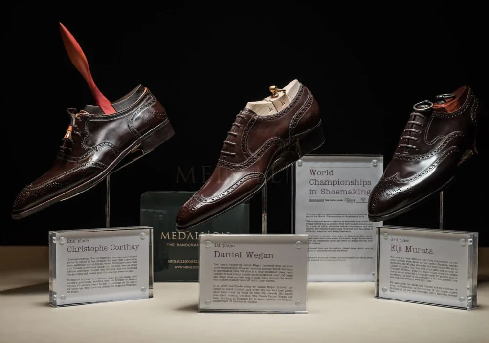 Three pairs of polished brown dress shoes displayed on stands, with plaques identifying the first, second, and third place winners of the World Championships of Shoemaking.