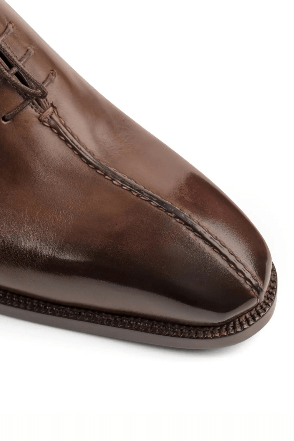 A close-up of a polished brown leather shoe featuring a pointed toe and detailed stitching.