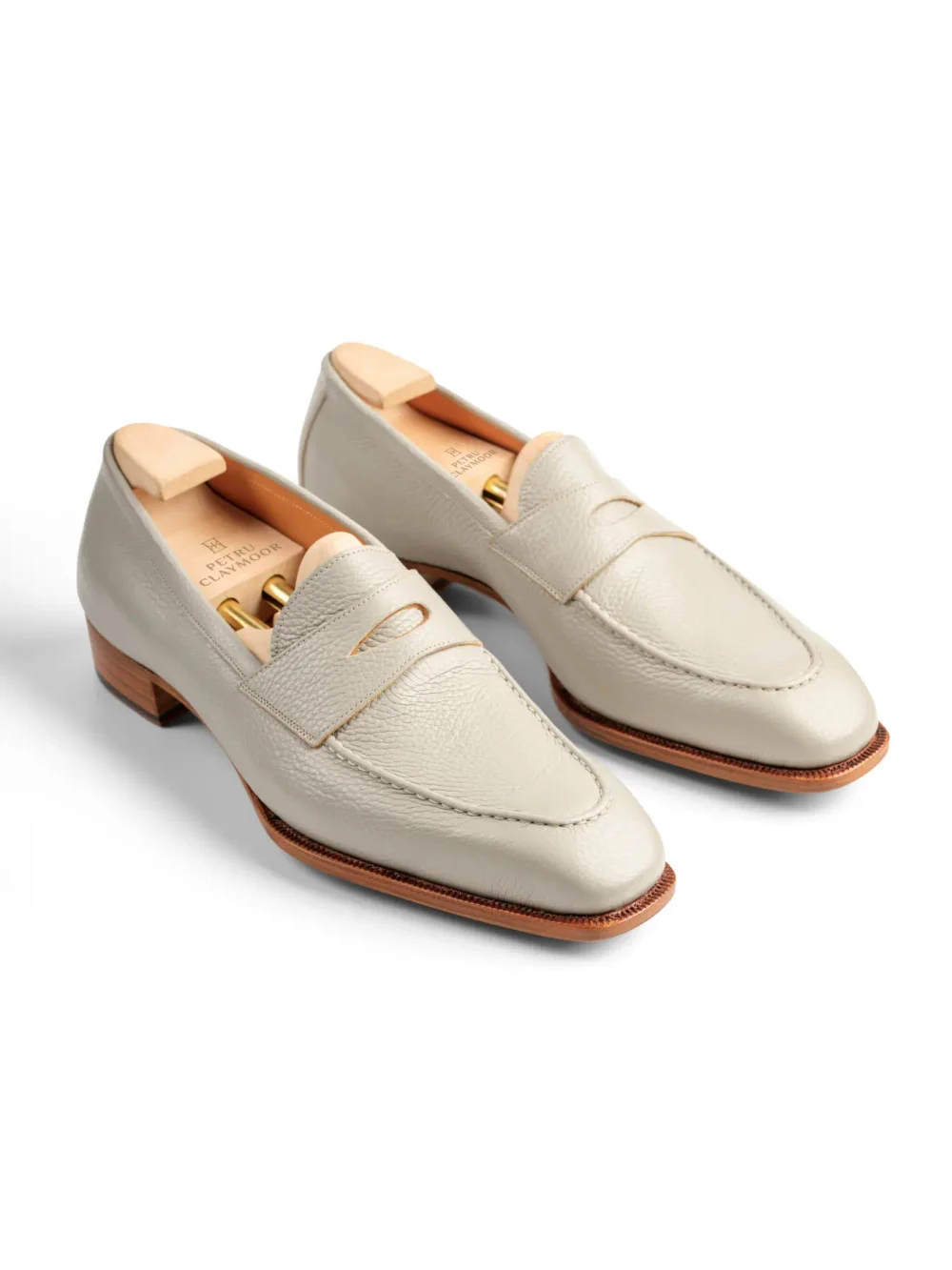 A pair of light beige leather loafers with a low heel and decorative stitching.