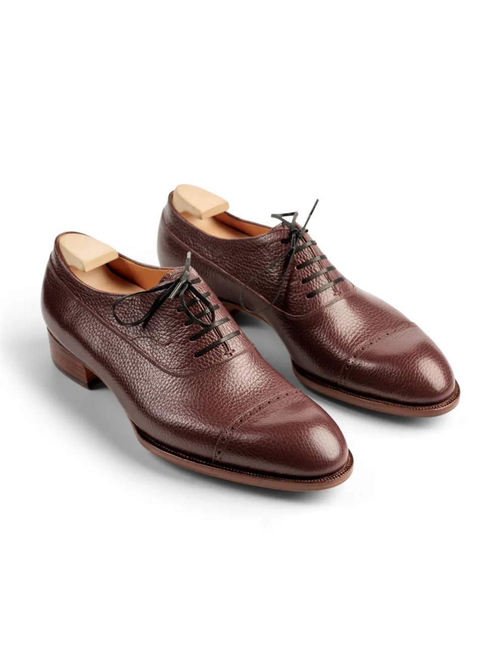 A pair of burgundy leather dress shoes with a textured finish and black laces.