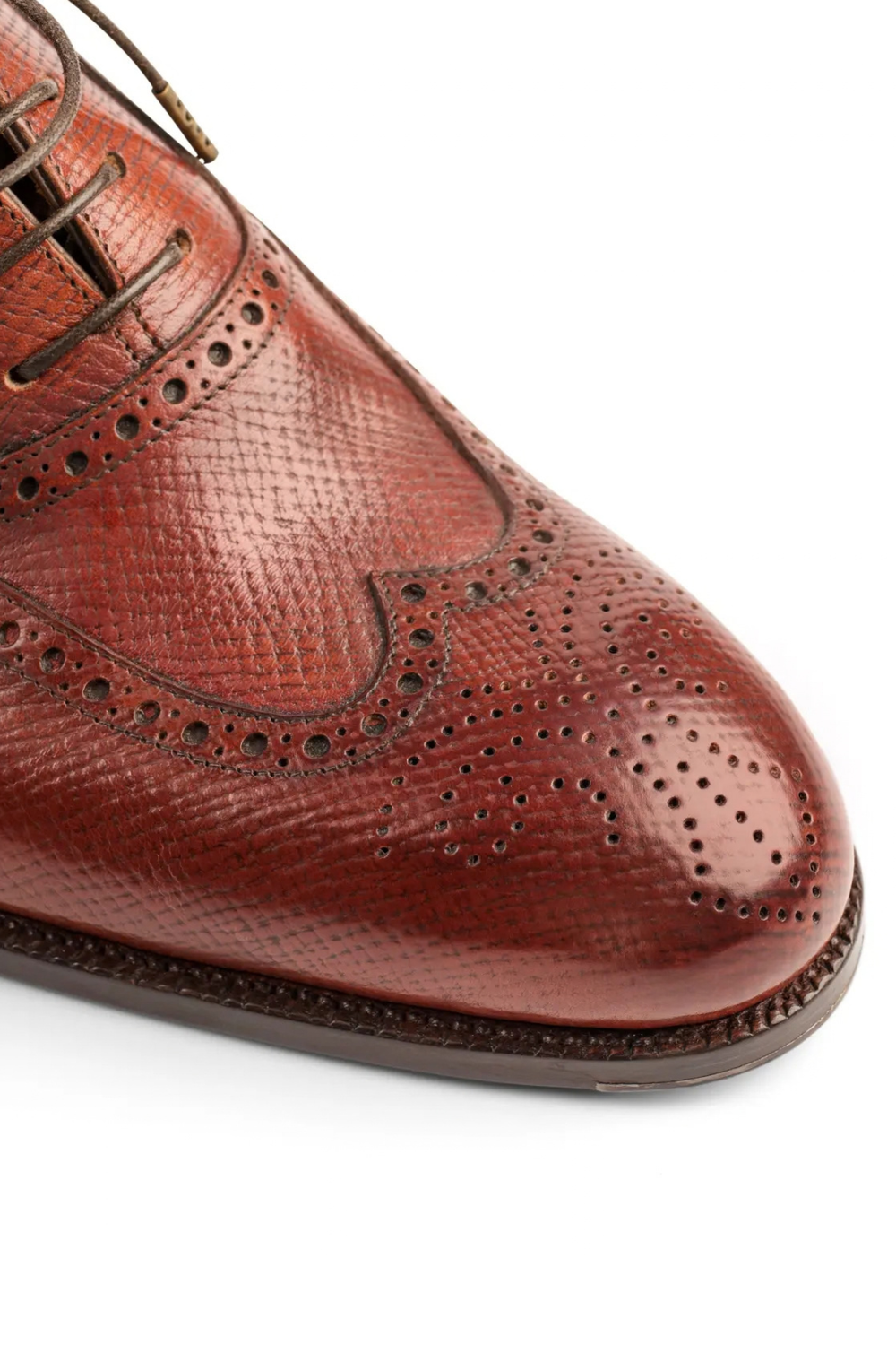 A close-up of a polished brown leather dress shoe featuring intricate brogue detailing.