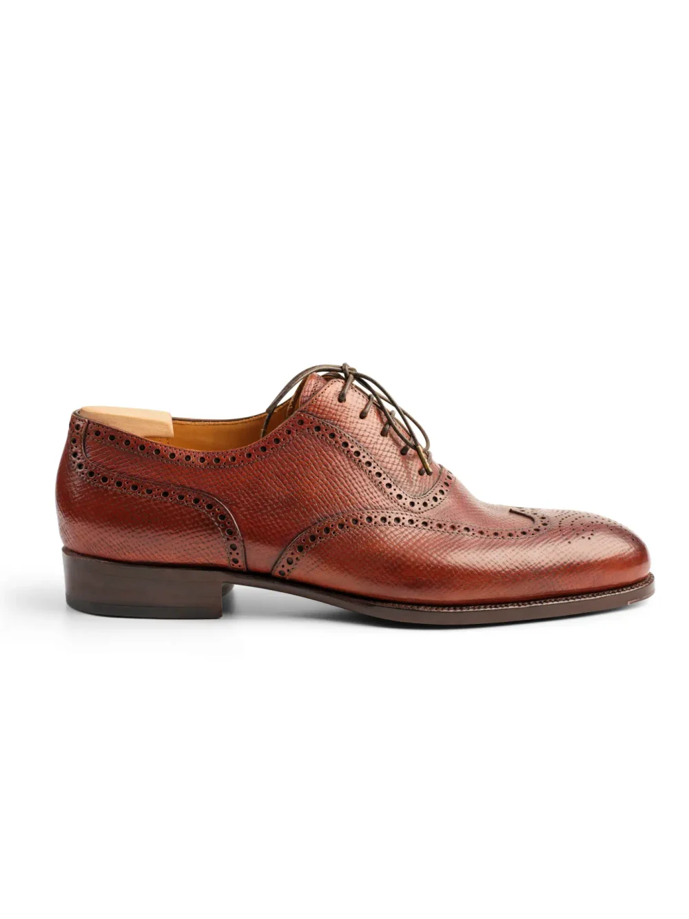 A brown leather dress shoe with brogue detailing and lace-up closure.