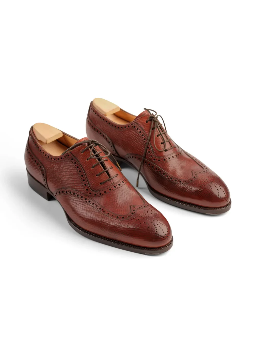 Brown leather dress shoes featuring brogue detailing and laces.