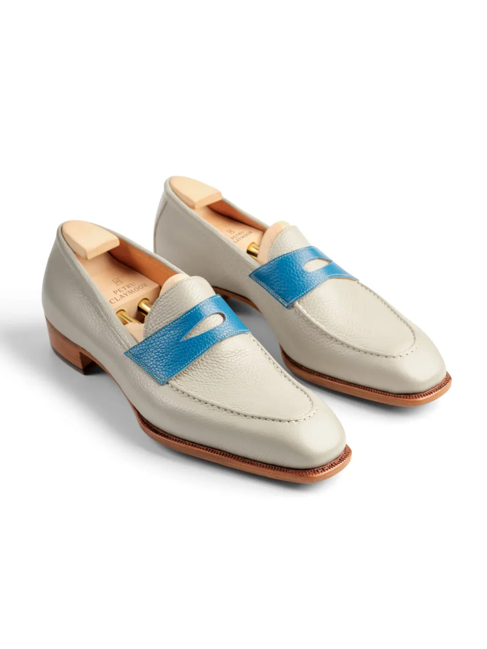 A pair of cream-colored loafers with a blue leather strap and wooden insoles.