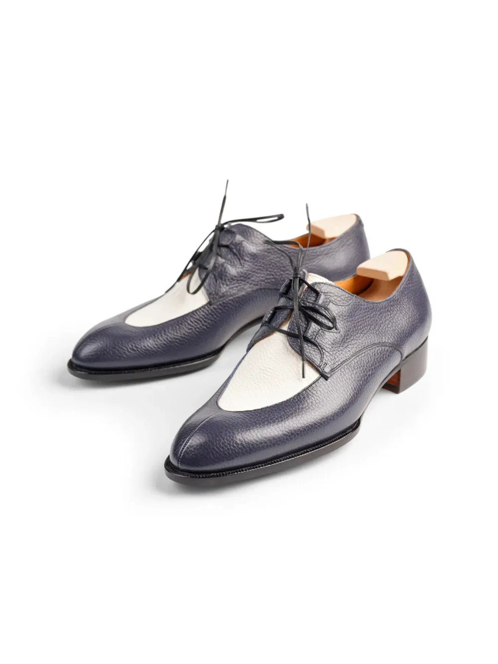 A pair of navy blue leather shoes with a cream-colored panel and black laces.