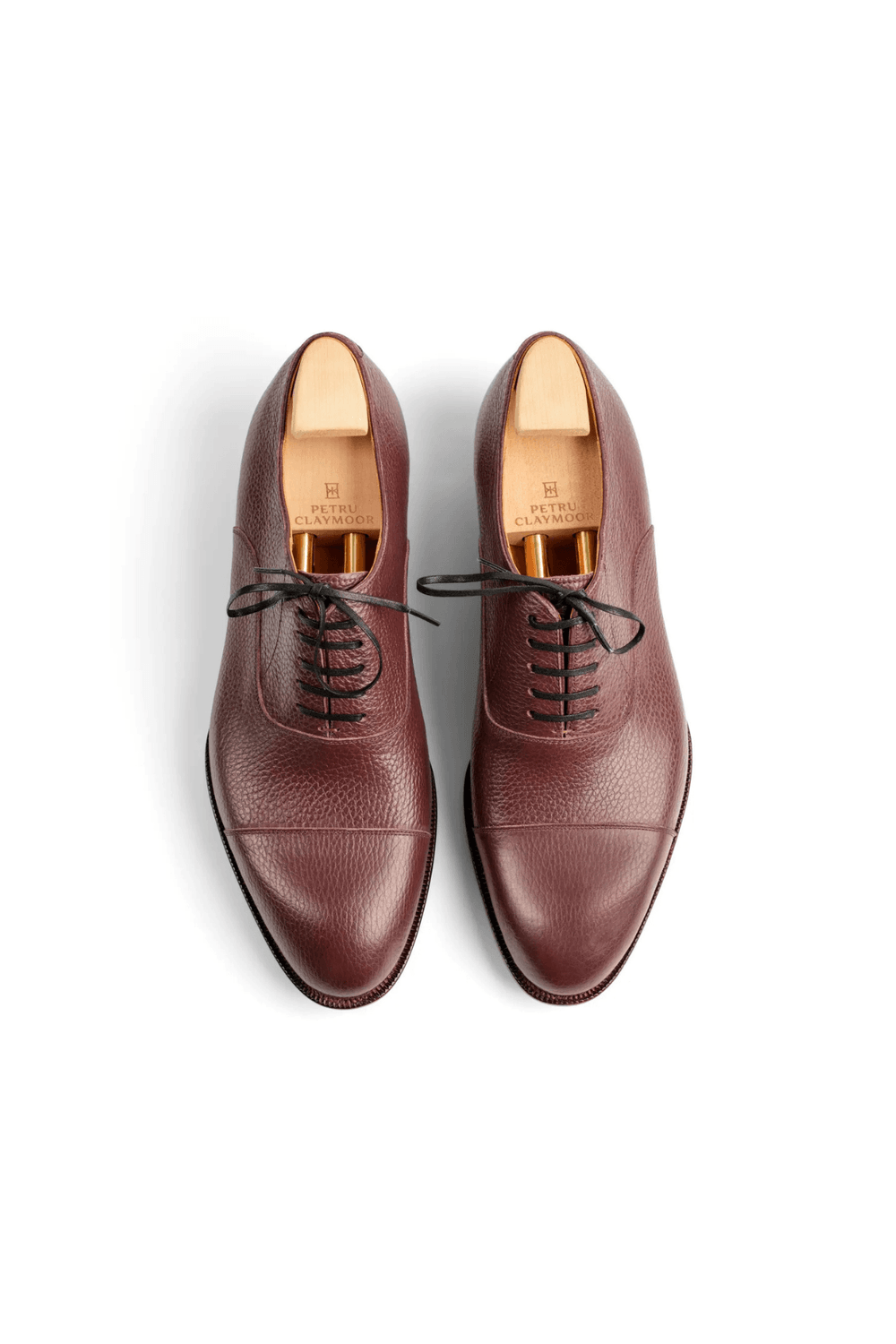 A pair of burgundy leather dress shoes with black laces and wooden shoe trees inside.