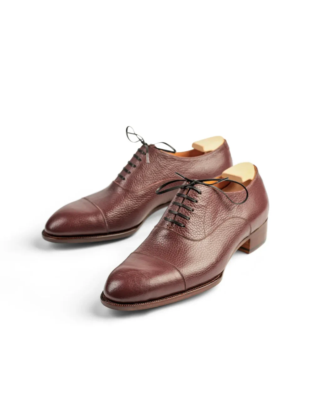 A pair of burgundy leather dress shoes with a textured finish and black laces.