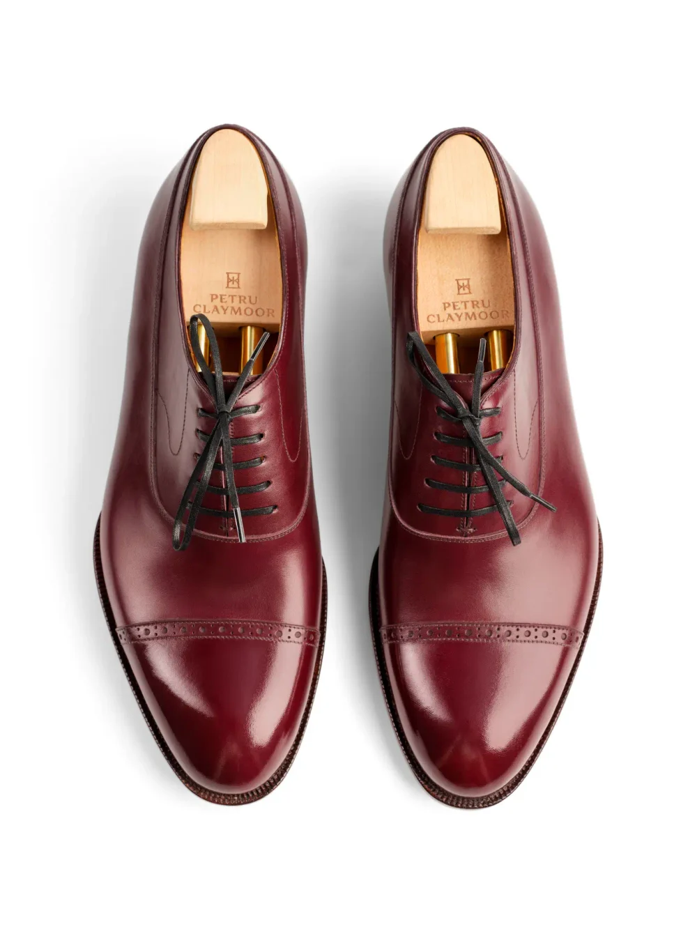 Two burgundy leather dress shoes with black laces and wooden shoe trees inside.