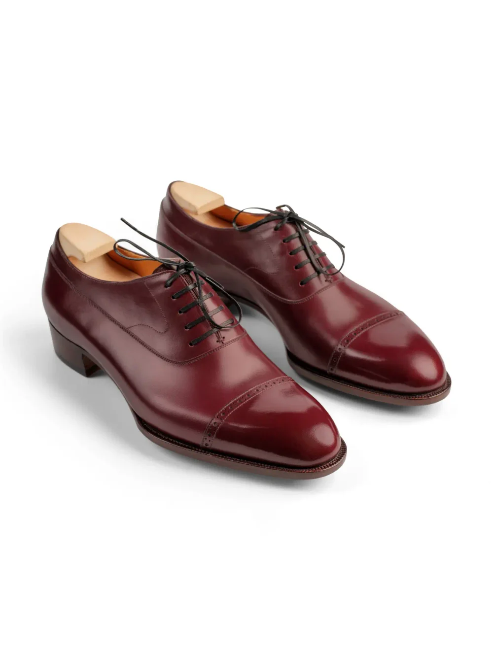 A pair of burgundy leather dress shoes with lace-up details and a cap toe design.