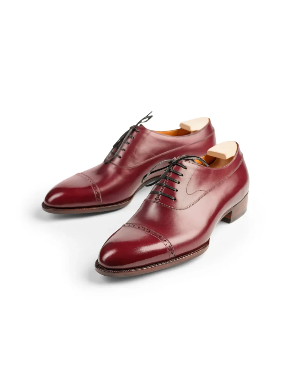 A pair of burgundy leather dress shoes with a cap toe and black laces.