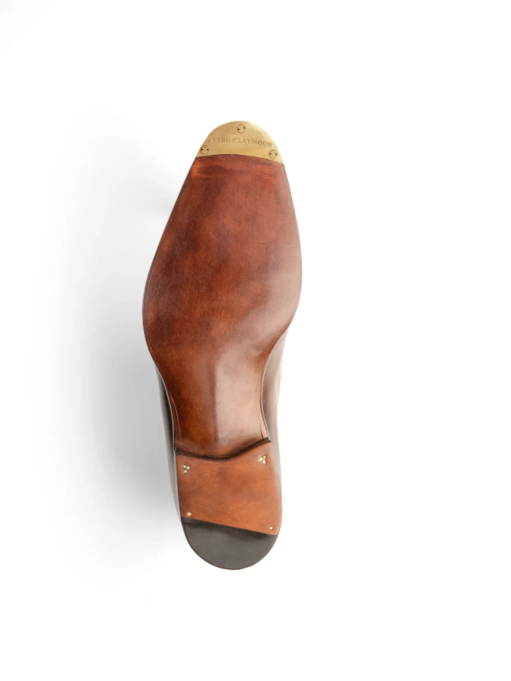 A close-up of the sole of a brown leather shoe with a brass logo plate that reads "Petru Claymoor."