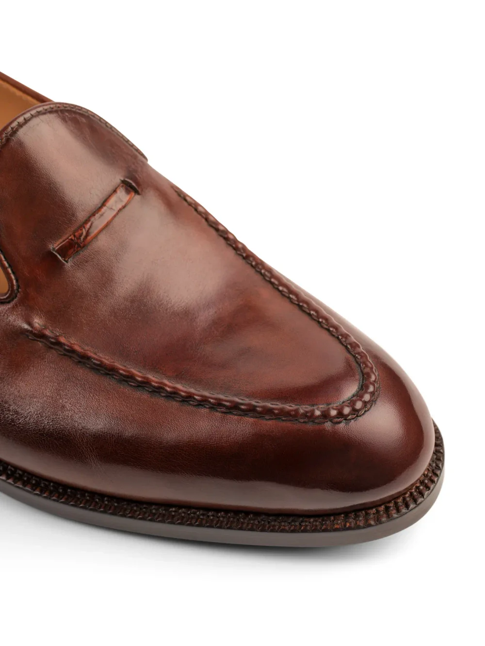 A close-up of a polished brown leather loafer with a decorative stitch along the edge.