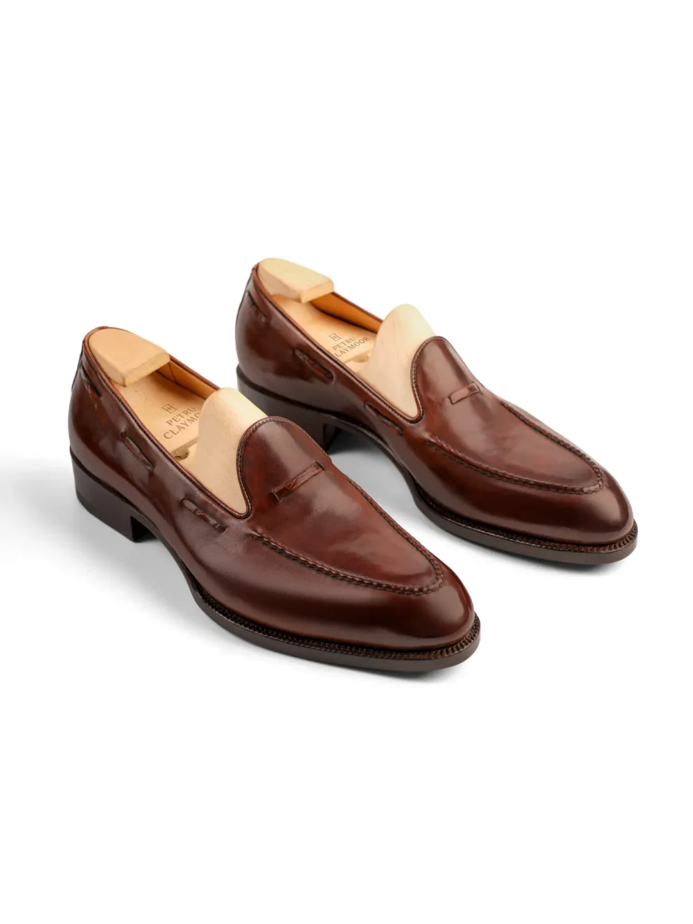 A pair of polished brown leather loafers with wooden shoe trees inserted.