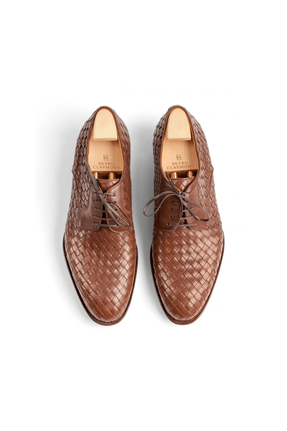 Two brown woven leather dress shoes with laces and wooden shoe trees inside.
