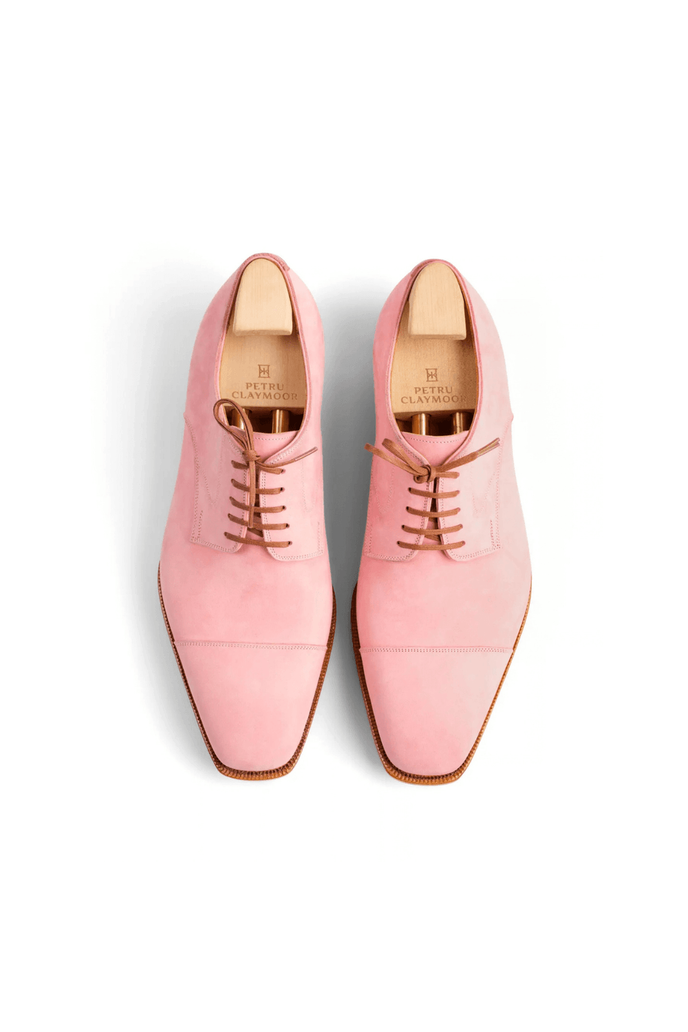 Pink suede dress shoes with brown laces and wooden shoe trees.