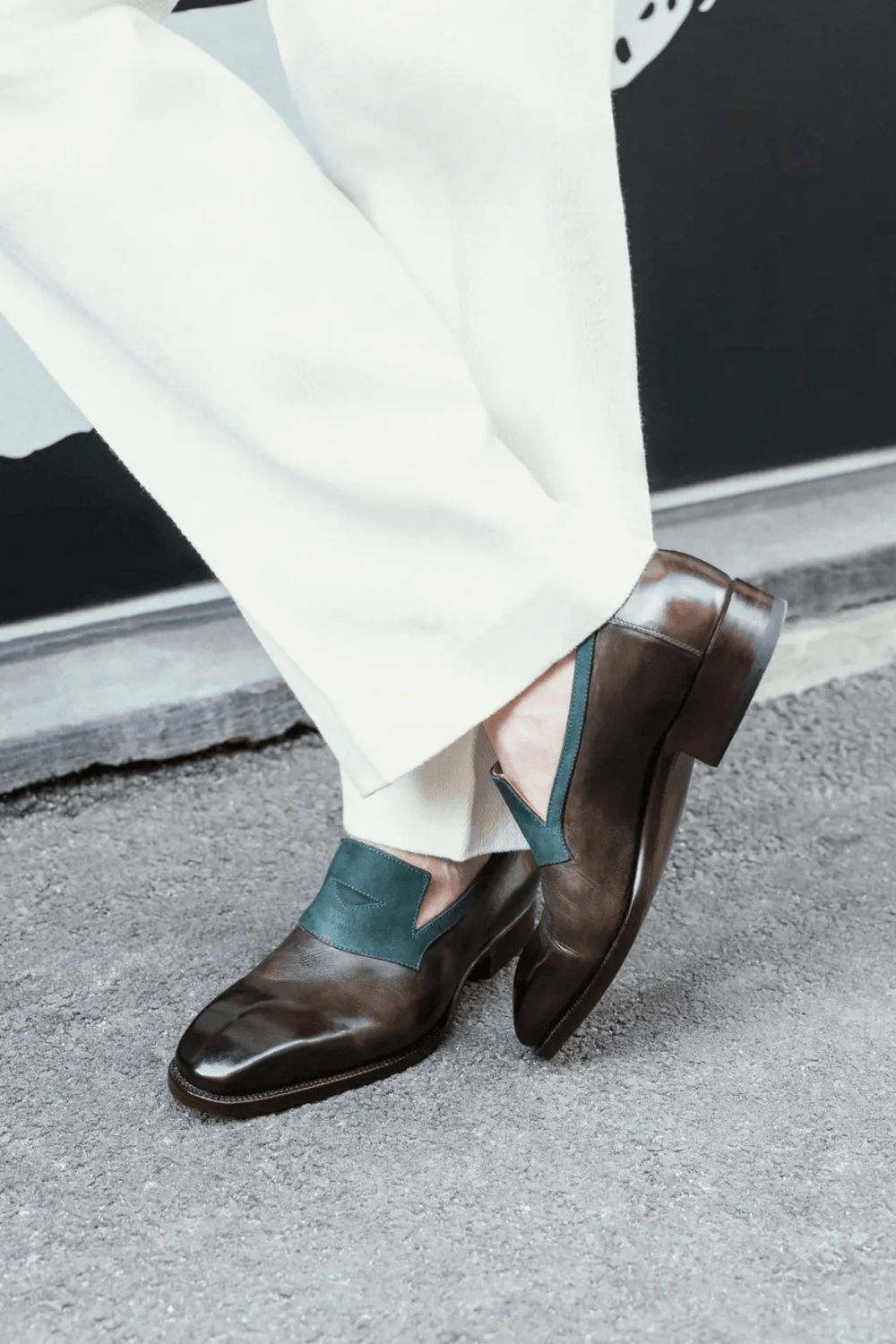 Brown leather shoes with green accents worn with white pants.