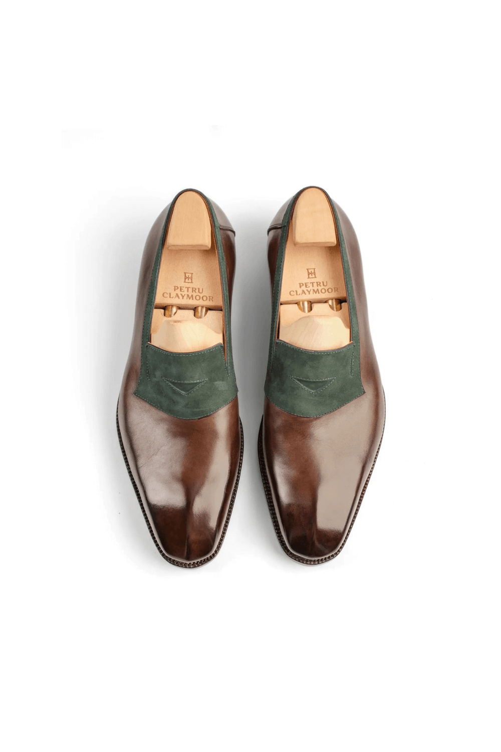 A pair of polished brown leather shoes with a green suede panel on the vamp.