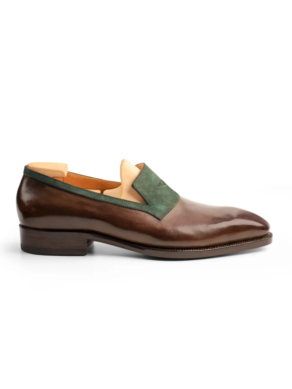 A brown leather shoe with a green suede accent on the vamp.