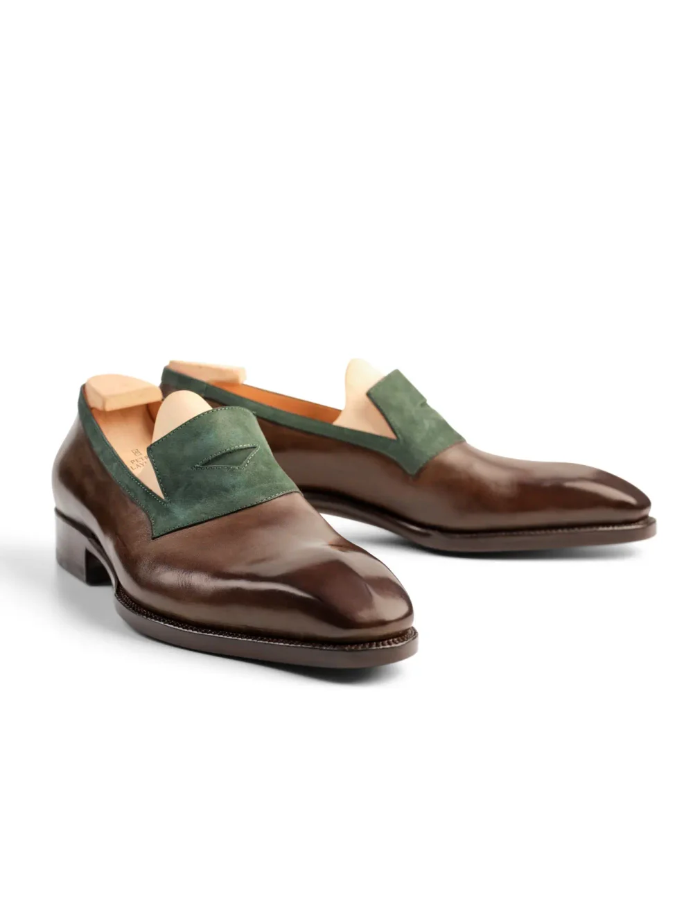 A pair of polished brown leather shoes with a green suede panel on the upper.