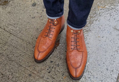 Brown leather shoes with laces, displaying water droplets, worn with dark jeans.