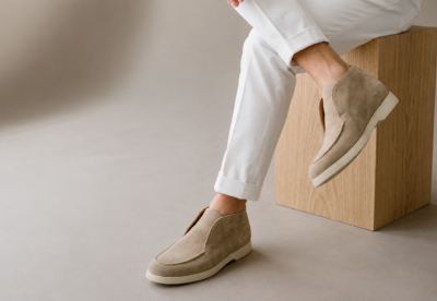 A close-up of a foot wearing a light brown suede slip-on shoe, paired with white cuffed pants.